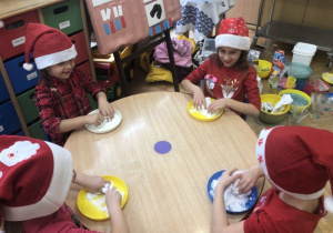 dzieci siedzą przy stolikach i mieszają sól z mąką na talerzykach